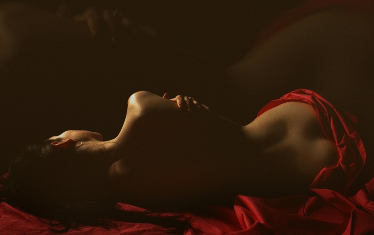Femme allongée dans une ambiance tamisée et élégante, drapée de tissu rouge.